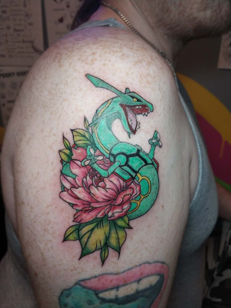 Green dragon coiled around a pink peony with green leaves, on a shoulder