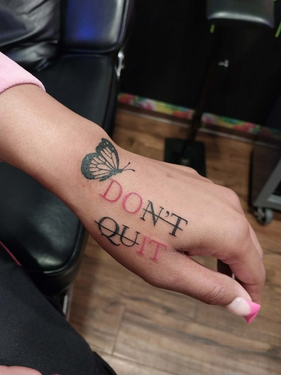 Lettering reading don't quit in black and red beneath a small butterfly, on a hand